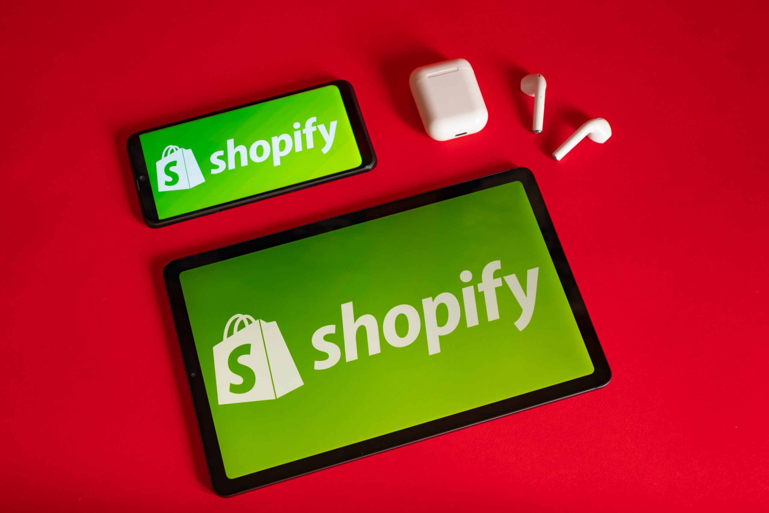 Tokio, Japan - June 05, 2022: Shopify web page displayed on a modern laptop, smartphone and notebook on red background. Shopify logo on iphone